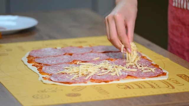 A female hand sprinkles a pizza with grated cheese close-up.