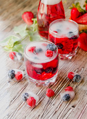 Summer berry lemonade with frozen berries on a wooden rustic table, selective focus