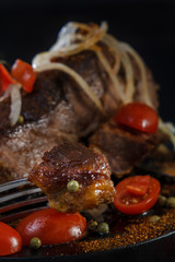 Fried lamb with vegetables. Fried meat on a black background. BBQ. Closeup. Piece of meat on the fork