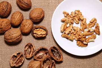 Opened and closed walnuts in a plate on a background of cloth and burlap