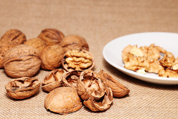Opened and closed walnuts in a plate on a background of cloth and burlap