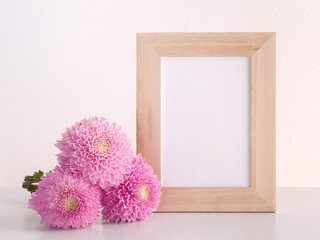Chrysanthemum flowers and blank photo frame on table in front of the wall. Filtered image.