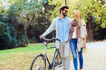 Young couple with bicycle walking in park on sunny autumn day.