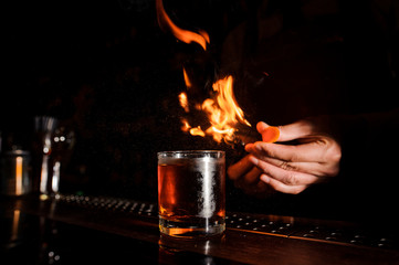 Glass of fiery cocktail on the dark bar counter