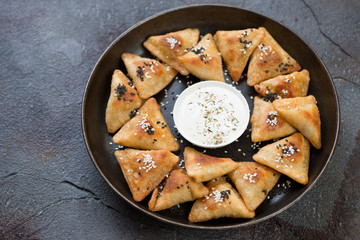 Metal plate with meat samosas and sauce on a cracked asphalt background, studio shot