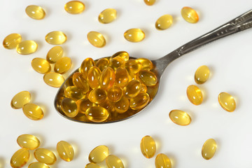 Omega-3 fish fat oil capsules in spoon on a white