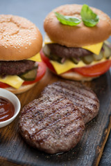 Close-up of two barbecued beef burger cutlets with hamburgers in the background, selective focus, shallow depth of field