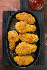 Metal plate with roasted breaded chicken wings on a black wooden serving board, above view, vertical shot