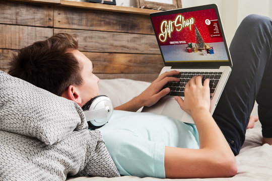 Man shopping christmas gifts with a laptop through internet while rest on the bed at home.