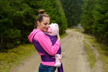 Happy young mother hugging baby in sling while outdoors