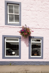 Fototapeta na wymiar fachada pintada de rosa con tres ventanas blancas y una maceta colgada en el muro con flores colgado.
