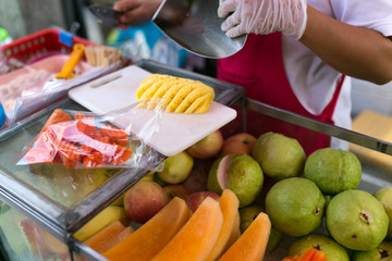 Women in red apron, latex glove cut pineapple. Fresh fruit, organic food. Guava, papaya