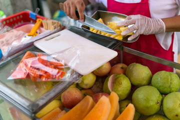Women in red apron, latex glove cut pineapple. Fresh fruit, organic food. Guava, papaya