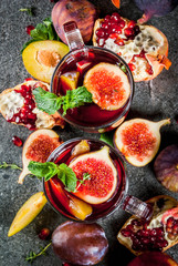 Warming autumn, winter cocktail drinks recipes. Hot red fruit sangria with apples, plums, figs, pomegranate, mint, cinnamon, thyme, lemon. On dark stone table, copy space top view