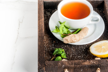 Cup of ginger tea with lemon,fresh mint and honey, in wooden tray, on white marble table, copy space