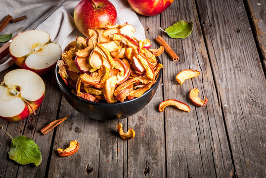 Homemade sun-dried organic apple slices, crispy apple chips, on an old rustic wooden table with fresh apple and cinnamon. Copy space
