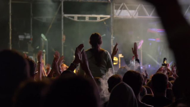 Handheld shot of many young people taking photographs with touch smart phone during a music entertainment public concert.Audience with hands raised at music festival at night.