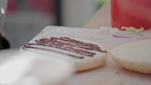 Closeup slow motion shot of chef preparing tasty burgers at outdoor stand. Sauce barbecue, fast food industry and unhealthy lifestyle concept.