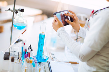 Professional young scientist using digital tablet while making experiment in chemical laboratory