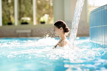 Fototapeten Serene girl enjoying stream of waterfall and its gentle splashes in swimming-pool at spa resort © pressmaster