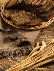 rye bread in a wicker tray with a napkin and spikelets on wooden surface, view from above