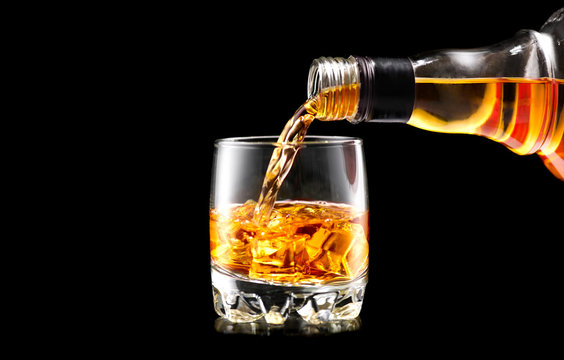 Whisky pouring from the bottle over black background. Whiskey on the rocks