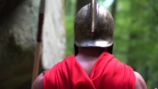 Close up rearview shot of a spartan warrior in battledress posing outdoors flexing his muscles strength power masculinity courage cape helmet protection fighting concept.