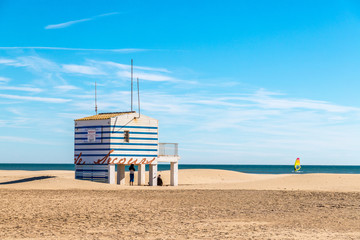 un poste de secours sur la plage, avec des rayures bleues, sur pilotis et une planche à voile au...
