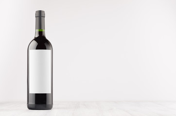 Dark wine bottle with blank white label on white wooden board, mock up. Template for advertising, design, branding identity.