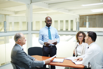 Group of modern traders listening to report of their colleague at meeting or seminar