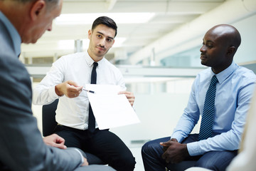Young economist pointing at contract or financial paper between his two colleagues