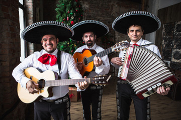 Mexican musicians mariachi near a Christmas tree.