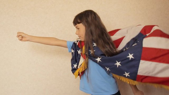 A child is playing with the US flag. A little girl is playing in an American super hero.