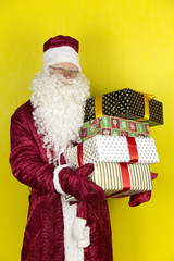 Santa Claus with gifts. Cheerful Santa Claus holds gifts in hands on a yellow background.