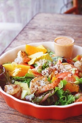 Fresh fruit salad with grilled shrimp and salad dressing served on red bowl.