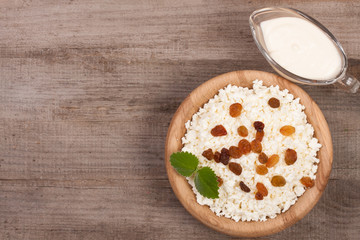 Cottage cheese in bowl with sour cream and raisins on old wooden background with copy space for your text. Top view