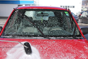 Red car is washed with a soapy brush at a coin operated car jet wash.