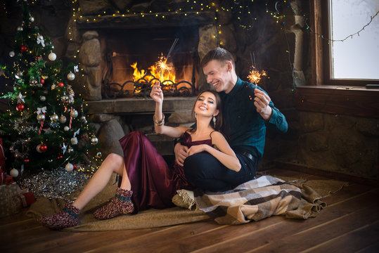 Joyful couple near christmas tree and fireplace with bengal lights selebrate New Year