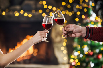 Celebreating christmas and new year. Couple keeps and toasts wine glasses near fireplace