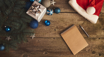 Christmas tree with gift box, decorations, red hat and notebook over wood  board