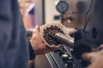 Close up male worker keeping bowl and special equipment with beans coffee. Control concept