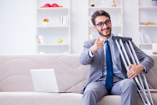 Businessman With Crutches And Broken Leg At Home Working