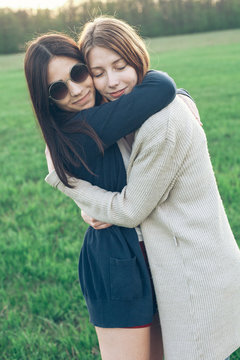 Two cheerful girls hugging on a glade under sunlight