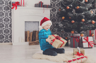 Cute boy in santa hat unwrapping christmas presents