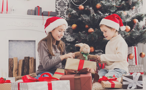 Happy children in santa hats unwrapping christmas presents