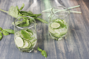 Glasses of cucumber detox water. Homemade cold gin tonic with basil on wooden table