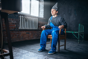 Afraided man in aluminum foil helmet sits in chair