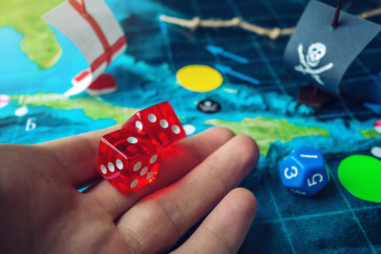 Hand throwing red dice on the world map of the playing field handmade Board games with a pirate ship