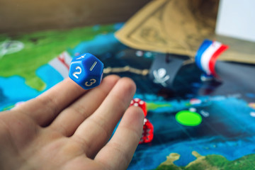 Hand rolls the blue dice on the world map of the playing field handmade Board games with a pirate ship