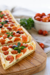 Rectangular tart with cherry tomatoes, ricotta, thyme, origan and black olives on rustic wooden cutting board on a linen cloth. Rustic style. Mediterranean cuisine.